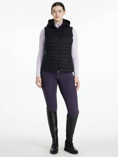 Woman wearing a black puffer vest, purple riding pants, and black riding boots 